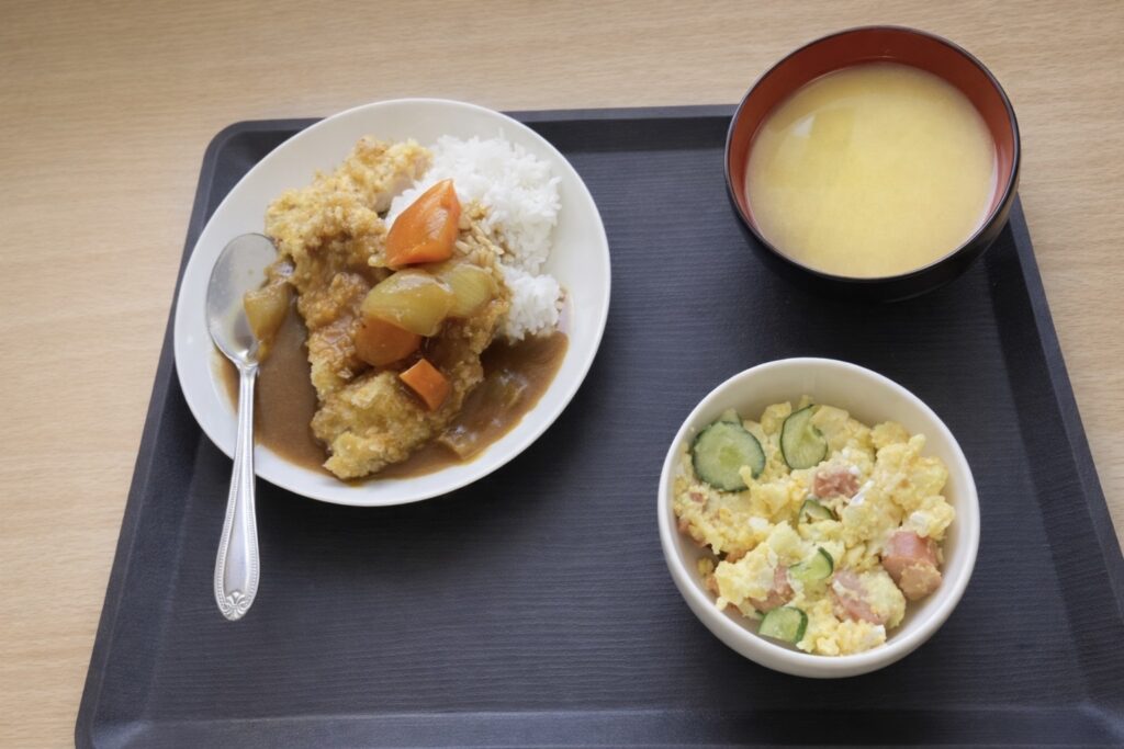 カツカレー、ポテトサラダ、コーンスープがおぼんにのっている画像