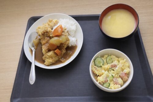 カツカレー、ポテトサラダ、コーンスープがおぼんにのっている画像